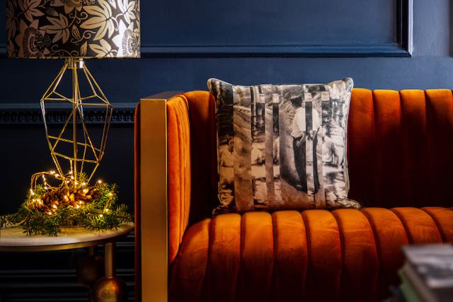 Orange upholstered sofa against a deep navy painted wall. Patterned cushion and lampshade on a side table