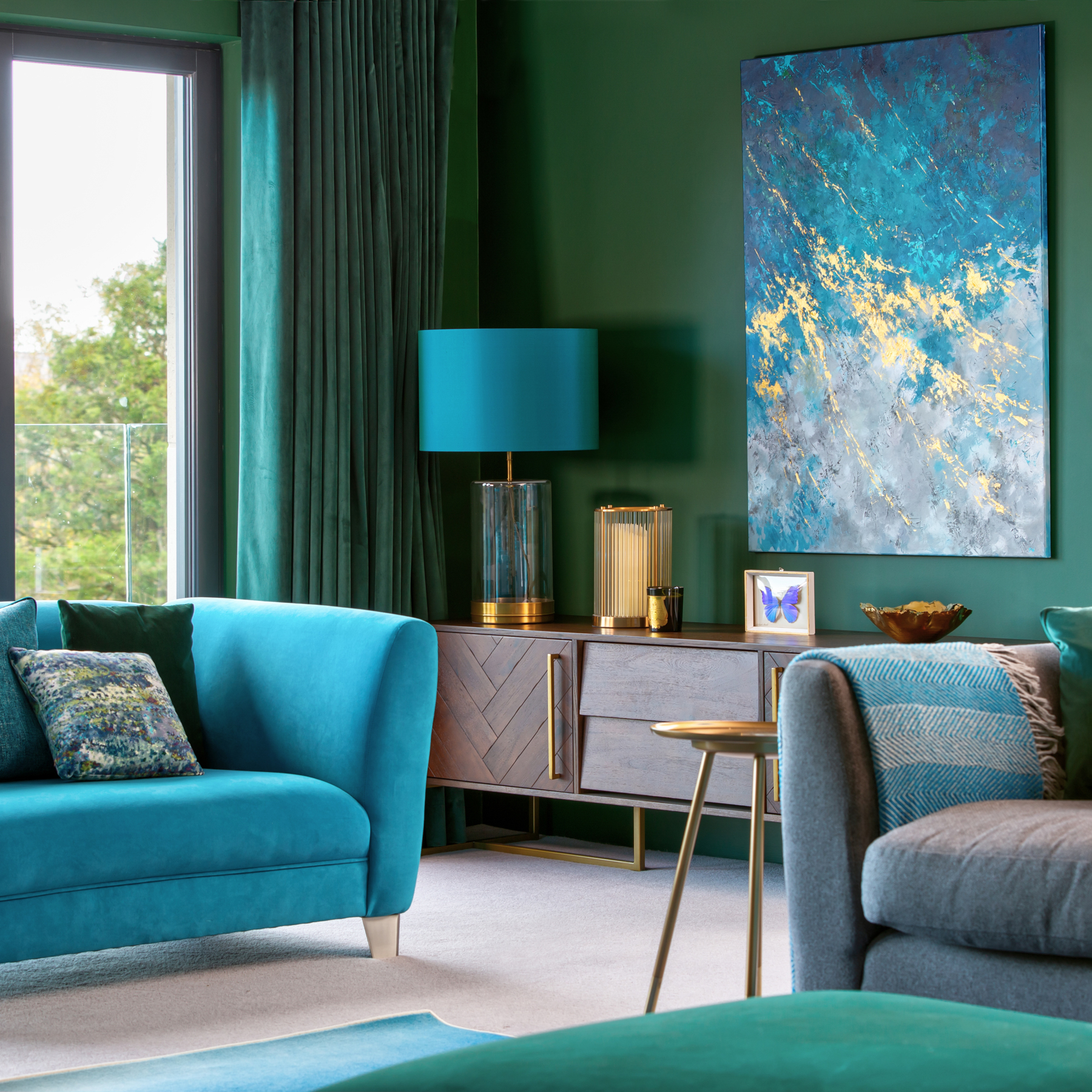 Contemporary living room green walls, teal blue sofa, sideboard with statement lamp