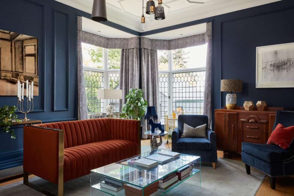 Sitting room with navy walls, pale grey carpet and oak floor, with orange sofa and navy armchairs and vintage sideboard