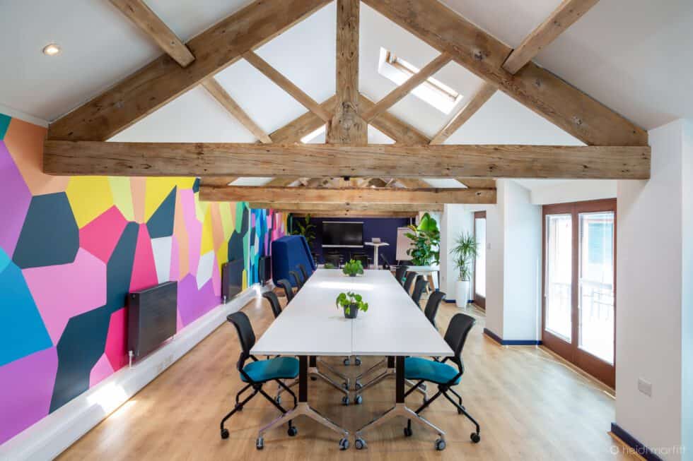 Open plan office in barn conversion with brightly coloured wallpaper and vibrant chairs on roller wheels