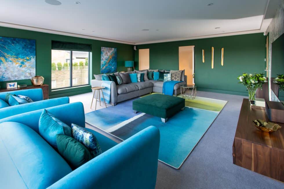 Bottle green walls contrast with turquoise armchairs and grey sofas in this generous sitting room