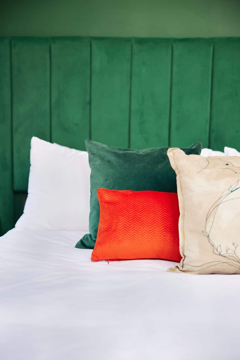 A bespoke oversized green headboard adds luxe to this master bedroom and a range of cushions on the bed adds interest