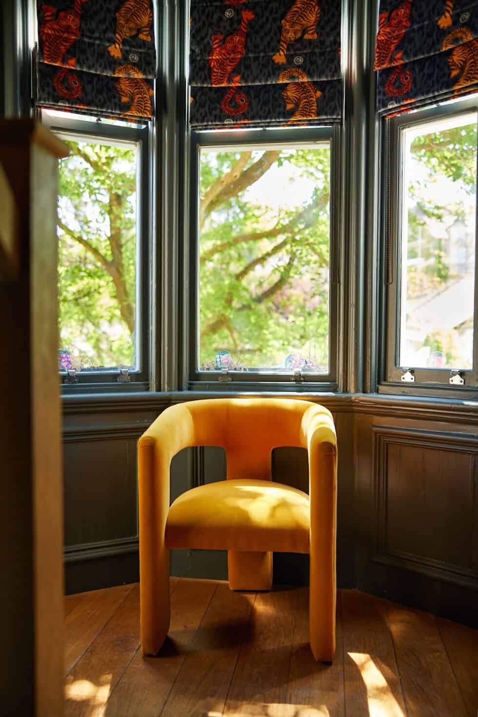 A mustard chair is a great addition to this dark grey hall while tiger patterned blinds add interest