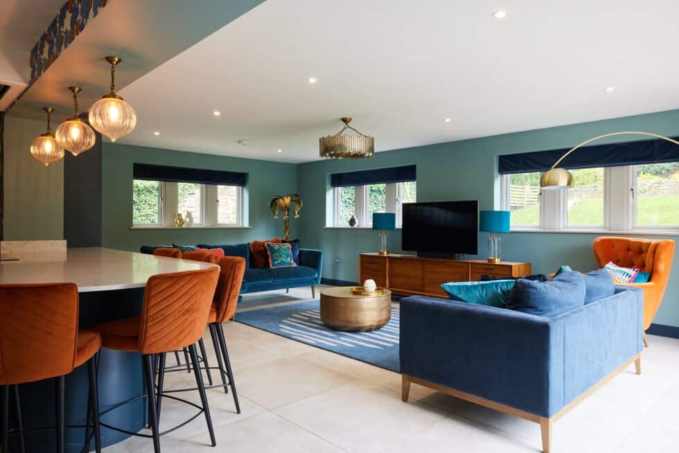 A well lit open plan kitchen and family room with navy sofas and orange chairs and sea green walls