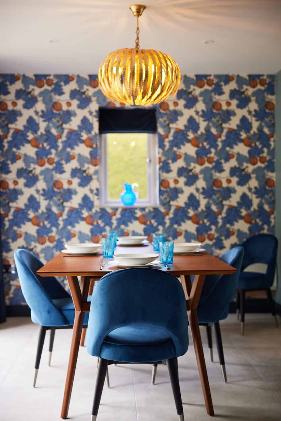 Patterned blue and orange wallpaper in this dining room complements the oak table and the upholstered blue dining chairs