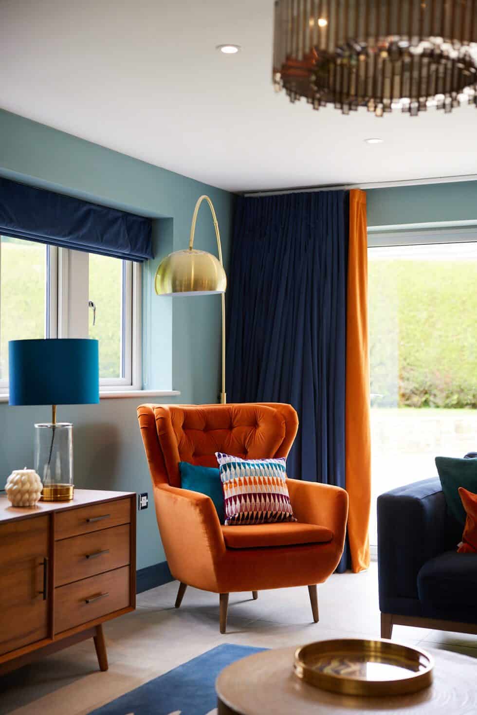 An orange armchair sits in a well lit family room with patterned cushions and bespoke navy blue curtains