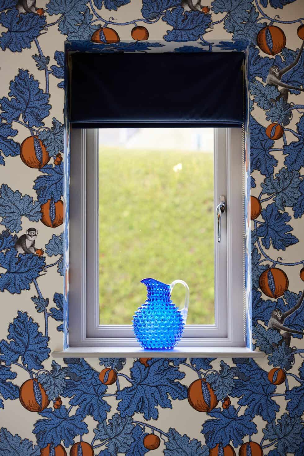 A bespoke navy blind complements the patterned wallpaper and the blue jug which sits on this window ledge