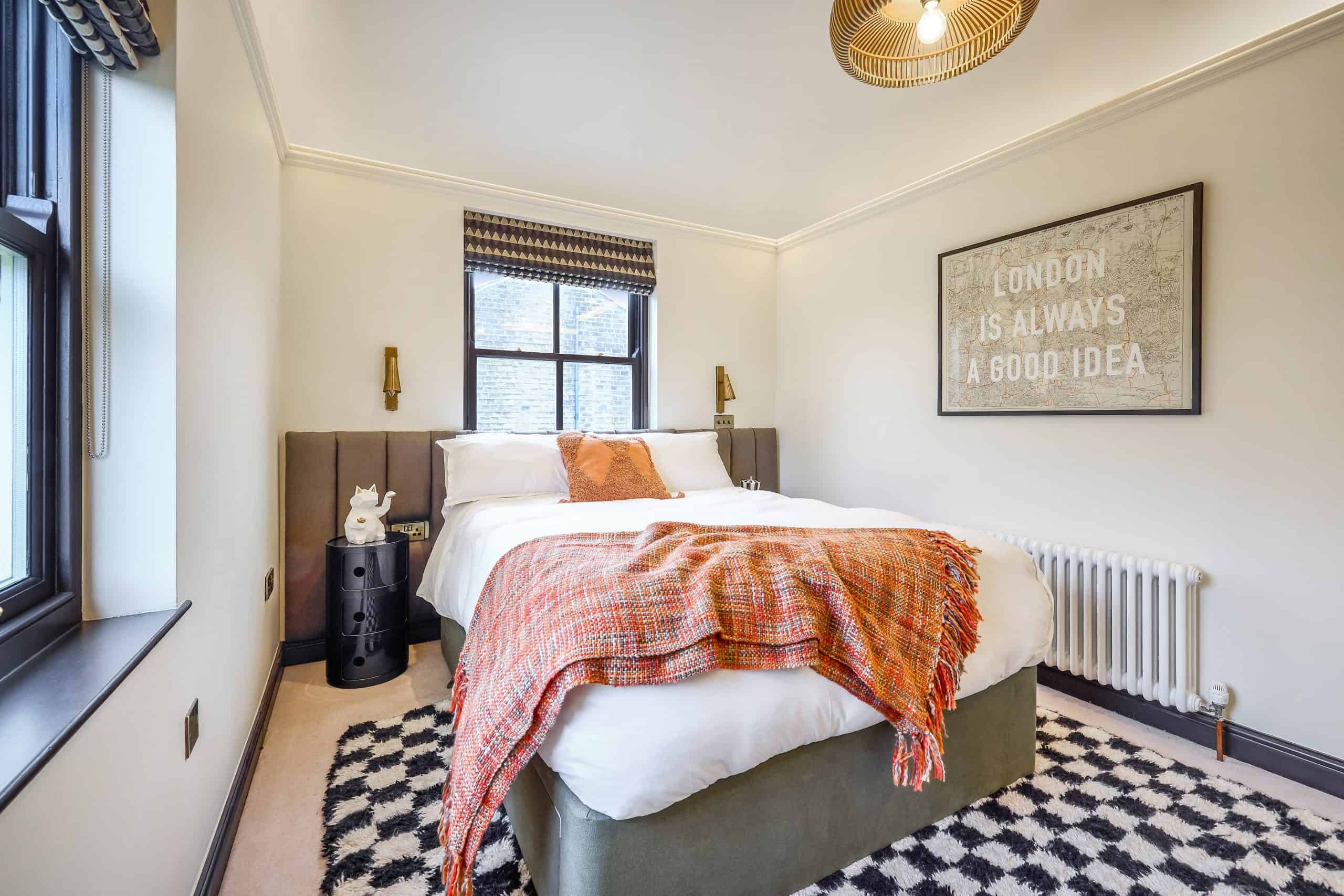 A burnt orange throw adds contrast to a monochrome bedroom with a checkered rug.