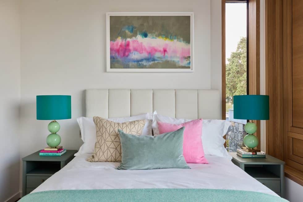 Neutral bedroom with mint blanket on the bed and mint table lamps with teal lampshades. Pink and white abstract painting above the bed ties in with the pink and mint cushions on the bed.