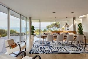 Contemporary dining room with cream armchair, walnut dining table and blue patterned rug with sea views beyond