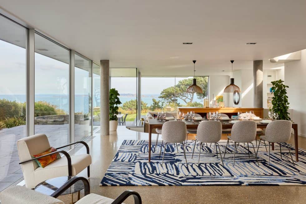 Contemporary dining room with cream armchair, walnut dining table and blue patterned rug with sea views beyond