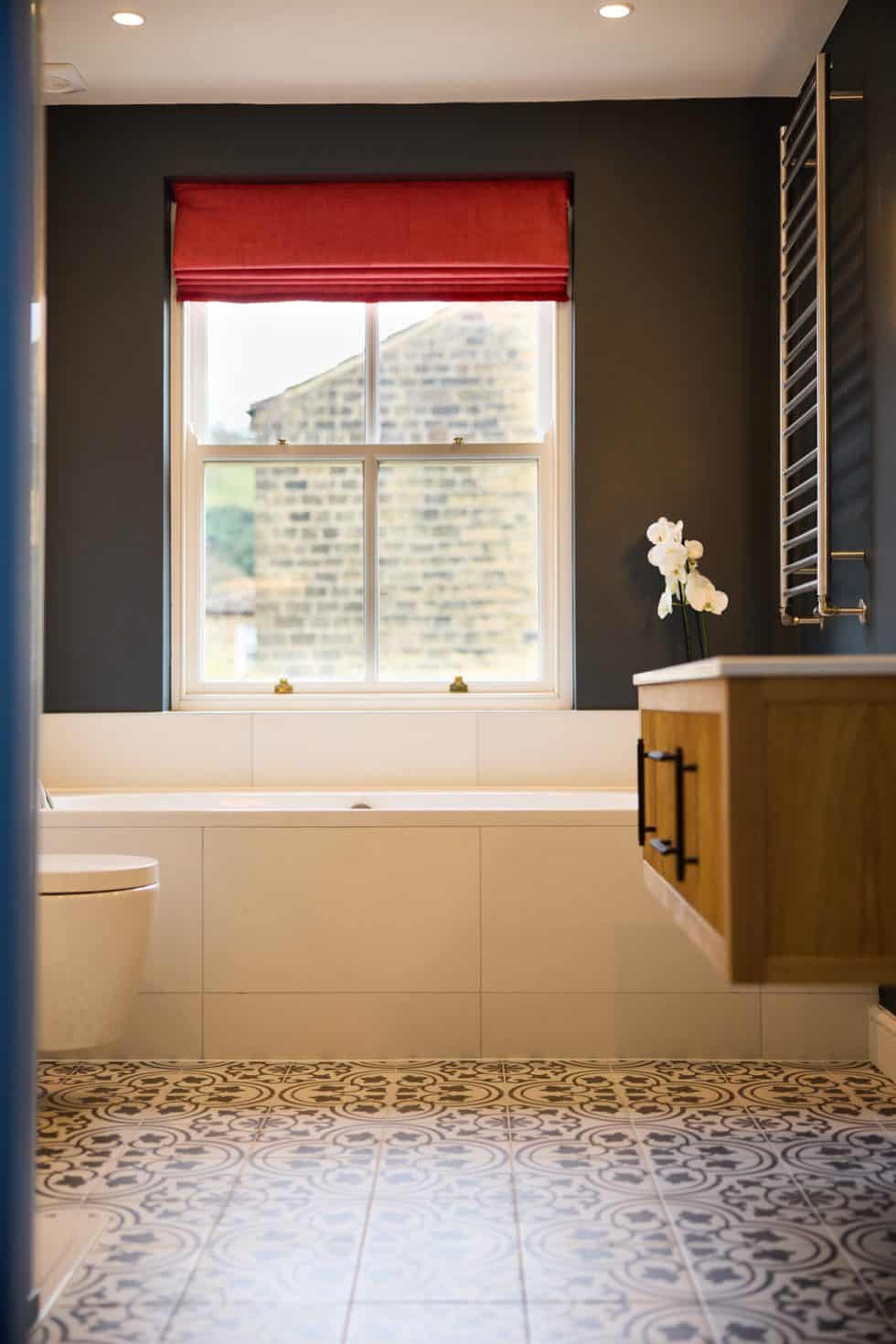 A rust blind complements this monochrome house bathroom where visual interest is added in the patterned floor tiles