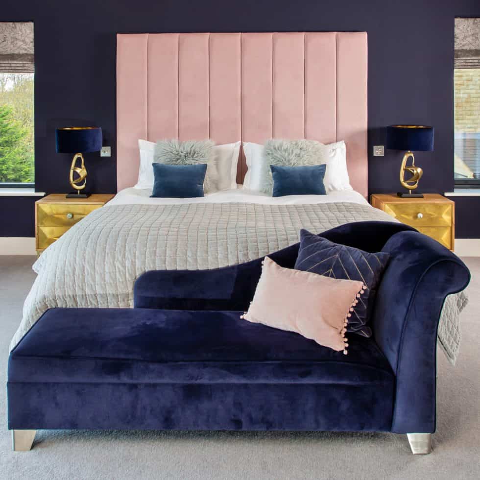 Rich navy walls and a navy chaise longue complement a bespoke pink headboard in this generous master bedroom
